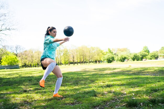 Retrato de mujer joven practicando habilidades futbolísticas y haciendo trucos con la pelota de fútbol