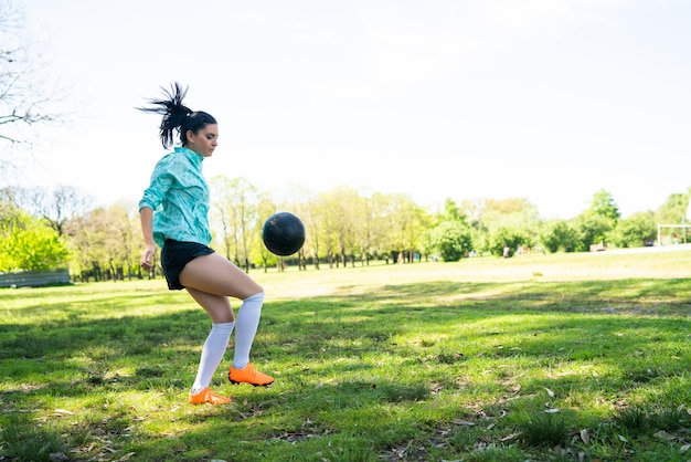 Retrato de mujer joven practicando habilidades futbolísticas y haciendo trucos con la pelota de fútbol