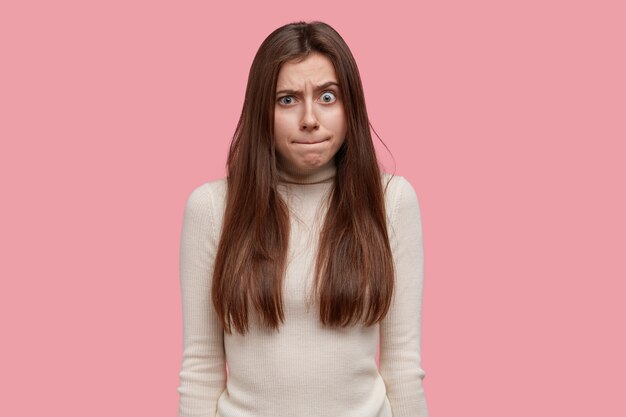 Retrato de mujer joven presiona los labios y se siente molesto y asombrado, levanta las cejas, está bajo tensión o presión