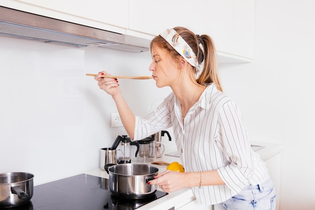 Foto gratuita retrato de una mujer joven probando la sopa mientras se prepara en la cocina