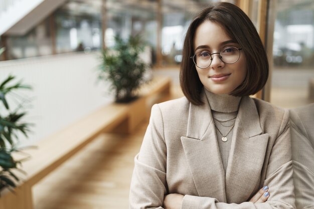 Retrato de mujer joven profesional y segura que trabaja en el comercio minorista, la industria empresarial, promover la empresa, unirse a su equipo de publicidad, sonriendo segura de sí misma y complacida en el soporte de la cámara en el pasillo.