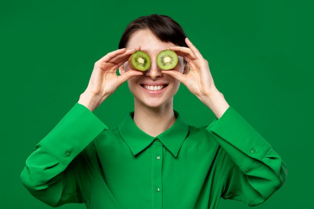 Retrato de mujer joven que cubre los ojos con kiwi