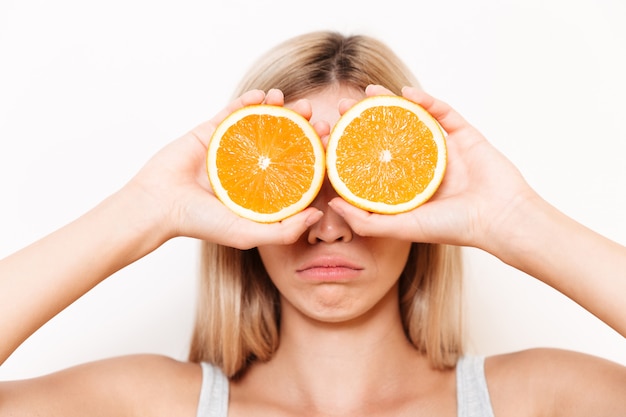 Retrato de una mujer joven que cubre sus ojos con fruta naranja