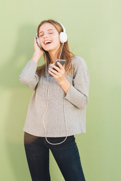 Foto gratuita retrato de una mujer joven que disfruta de la música en los auriculares contra el telón de fondo verde menta