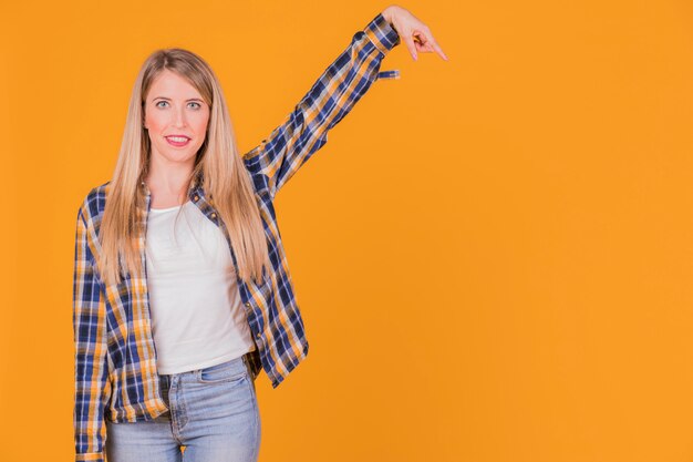 Retrato de una mujer joven que levanta sus brazos contra un contexto anaranjado