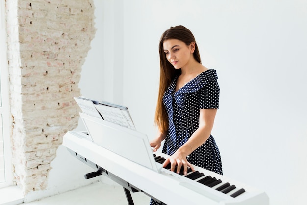 Retrato de una mujer joven que mira la hoja musical que toca el piano