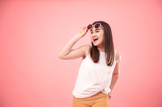 Retrato de una mujer joven que muestra emociones, con gafas en rosa aislado.