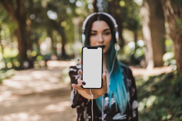 Retrato de la mujer joven que muestra el teléfono elegante blanco en blanco