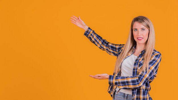 Retrato de una mujer joven que presenta algo sobre un fondo naranja