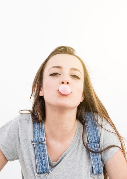 Retrato de una mujer joven que sopla goma de mascar rosa