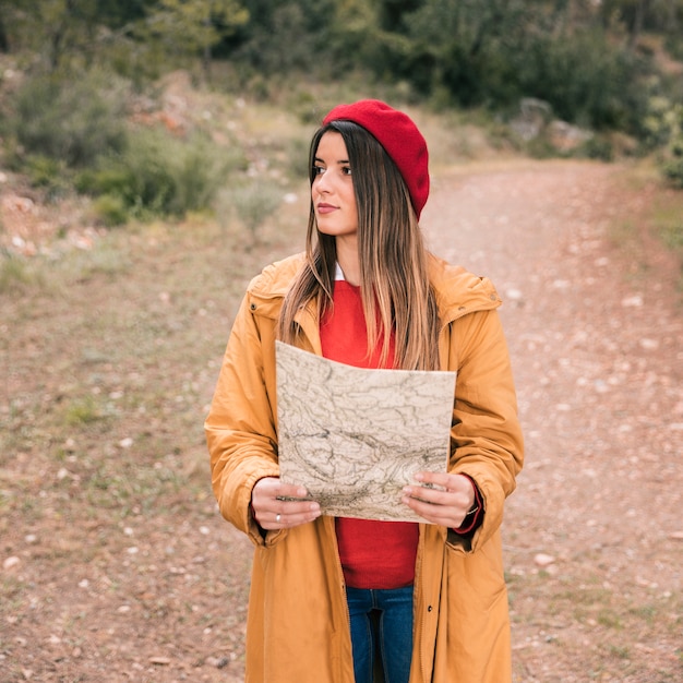 Foto gratuita retrato de una mujer joven que sostiene un mapa en la mano que se coloca en rastro