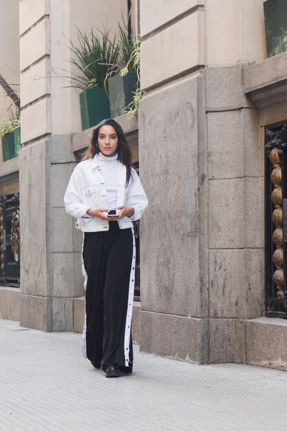 Retrato de una mujer joven que sostiene el teléfono móvil en la mano mirando a la cámara