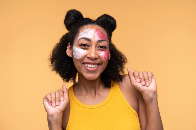 Retrato de una mujer joven que usa crema hidratante y mascarilla facial mientras se ve feliz