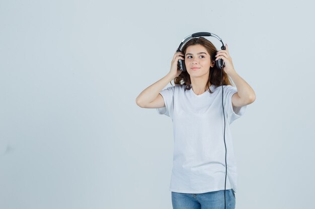 Retrato de mujer joven quitándose los auriculares con camiseta blanca, jeans y mirando la vista frontal de ensueño