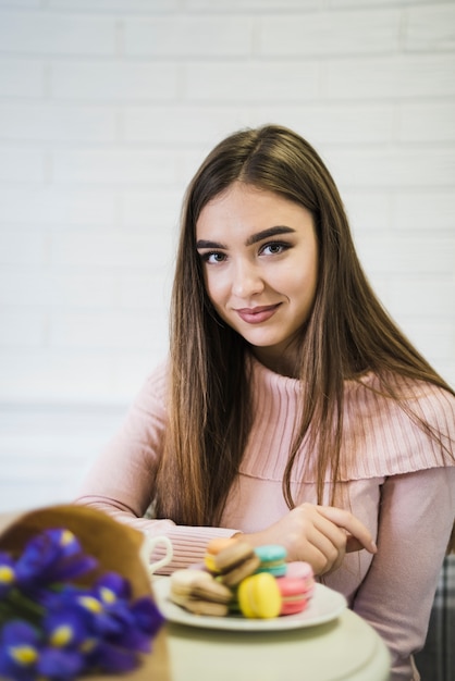 Foto gratuita retrato de una mujer joven con ramo de flores y macarrones en placa