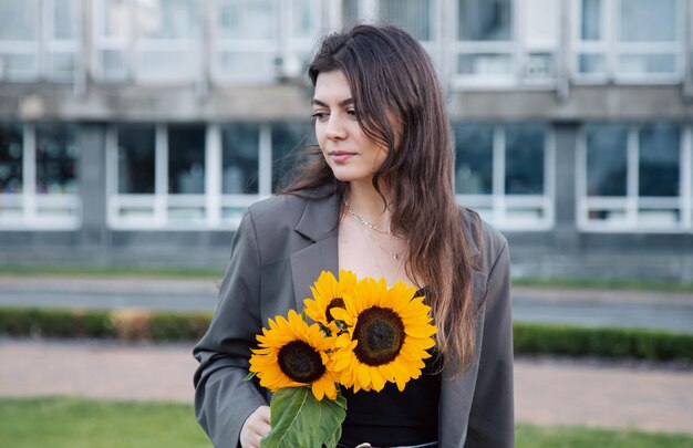 Retrato de una mujer joven con un ramo de girasoles en la ciudad