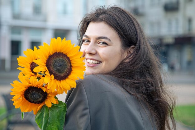 Retrato de una mujer joven con un ramo de girasoles en la ciudad