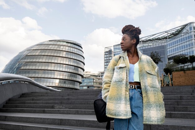 Retrato de mujer joven con rastas afro y mochila en la ciudad