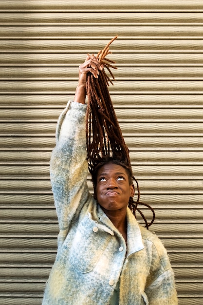 Foto gratuita retrato de mujer joven con rastas afro mostrando su cabello mientras está en la ciudad