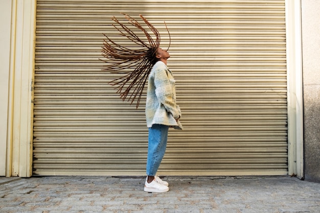 Retrato de mujer joven con rastas afro mostrando su cabello mientras está en la ciudad