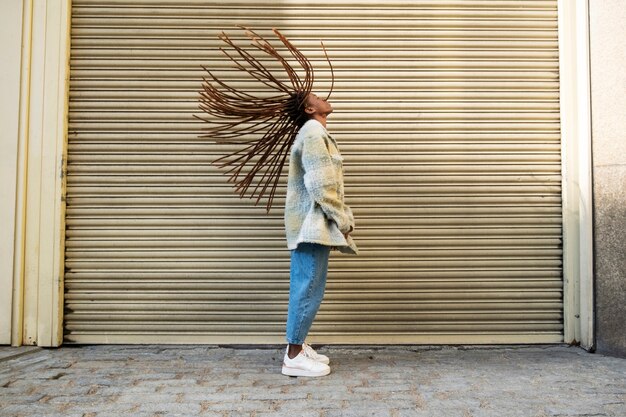 Retrato de mujer joven con rastas afro mostrando su cabello mientras está en la ciudad