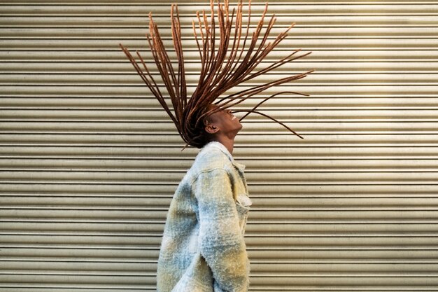 Retrato de mujer joven con rastas afro mostrando su cabello mientras está en la ciudad