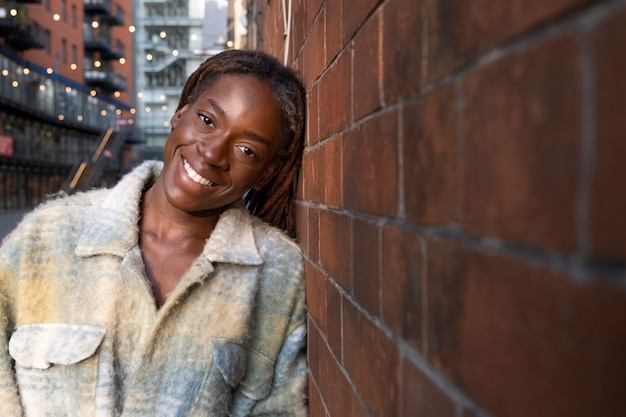 Foto gratuita retrato de mujer joven con rastas afro posando junto a la pared de ladrillo en la ciudad