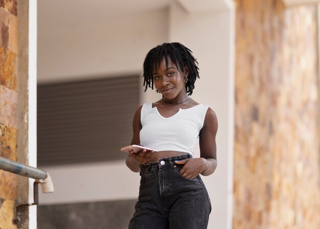 Retrato de mujer joven con rastas afro con smartphone al aire libre