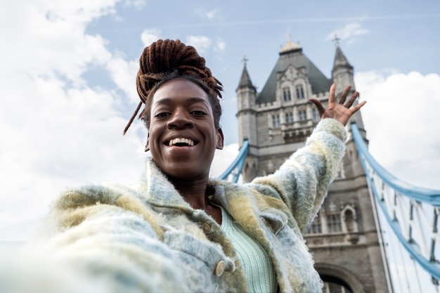 Retrato de mujer joven con rastas afro tomando un selfie al lado del puente en la ciudad