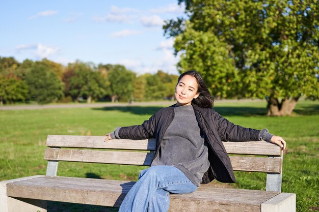 Retrato de mujer joven en ropa de exterior sentada en un banco relajado sonriendo y disfrutando de la vista en gre