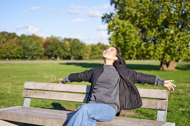 Retrato de mujer joven en ropa de exterior sentada en un banco relajado sonriendo y disfrutando de la vista en gre