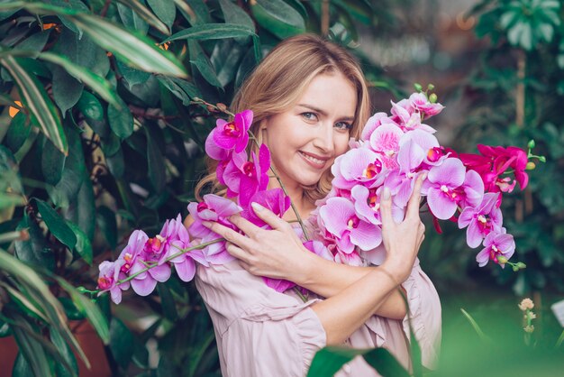 Retrato de una mujer joven rubia abrazando las ramas de flores de orquídeas