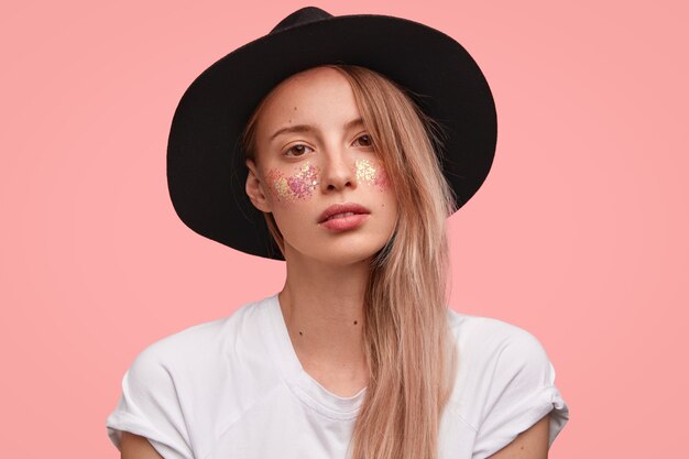 Retrato de mujer joven rubia con brillo en la cara y elegante sombrero