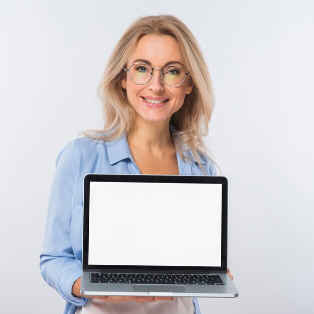 Retrato de una mujer joven rubia que sostiene una computadora portátil abierta con la pantalla en blanco contra el contexto blanco