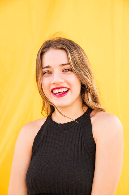 Retrato de la mujer joven rubia sonriente que se coloca delante de fondo amarillo