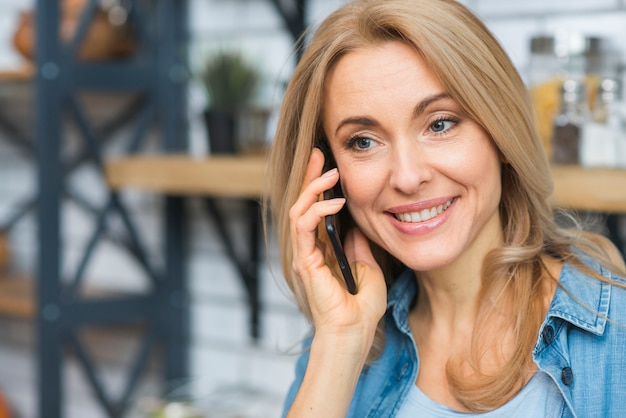 Foto gratuita retrato de una mujer joven rubia sonriente que habla en el teléfono elegante