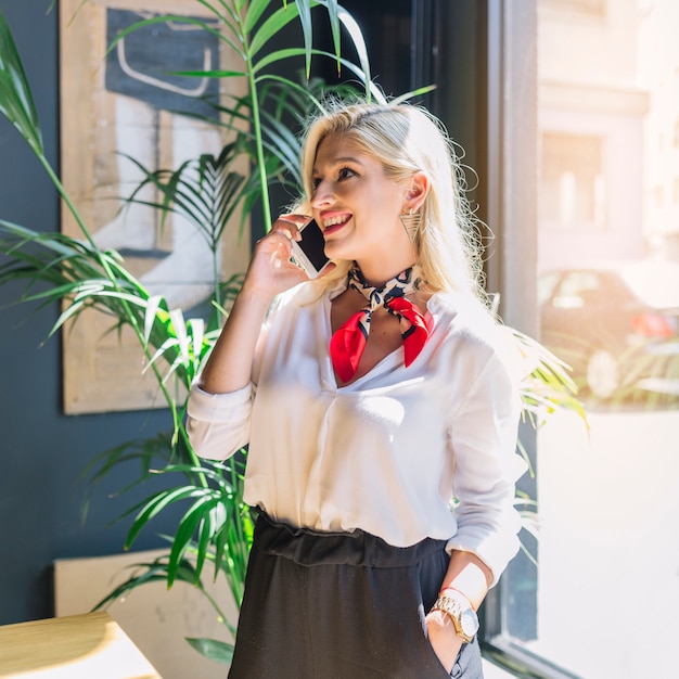 Retrato de una mujer joven rubia sonriente que habla en el teléfono móvil