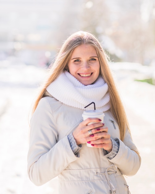 Retrato de la mujer joven rubia sonriente que sostiene la taza de café disponible