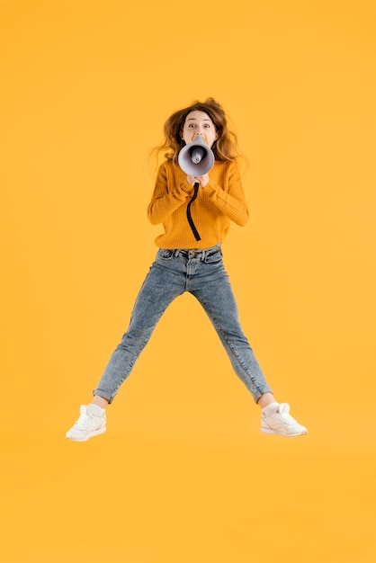 Retrato mujer joven saltando con megáfono