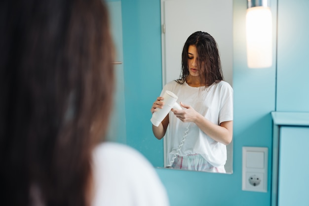 Retrato de mujer joven con secador de pelo en el baño.