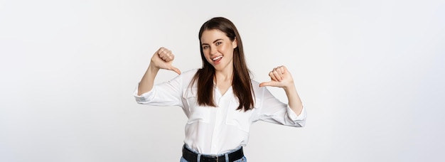 Foto gratuita retrato, de, mujer joven, señalar, en sí mismo, autopromoción, posición, encima, fondo blanco