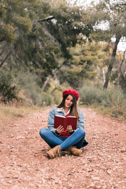 Retrato de una mujer joven sentada en el camino leyendo el libro