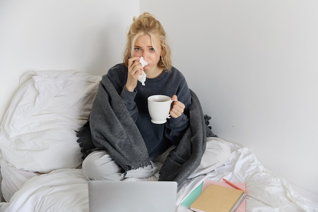 Foto gratuita retrato de una mujer joven sentada en casa enferma sintiéndose mal bebiendo té pasando tiempo en la cama