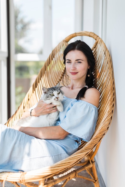 Foto gratuita retrato de mujer joven sentada con su gato en silla