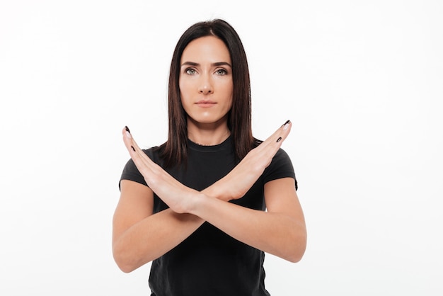 Foto gratuita retrato de una mujer joven seria que muestra gesto de manos cruzadas