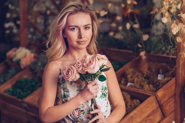 Foto gratuita retrato de una mujer joven seria que sostiene rosas rosadas disponibles