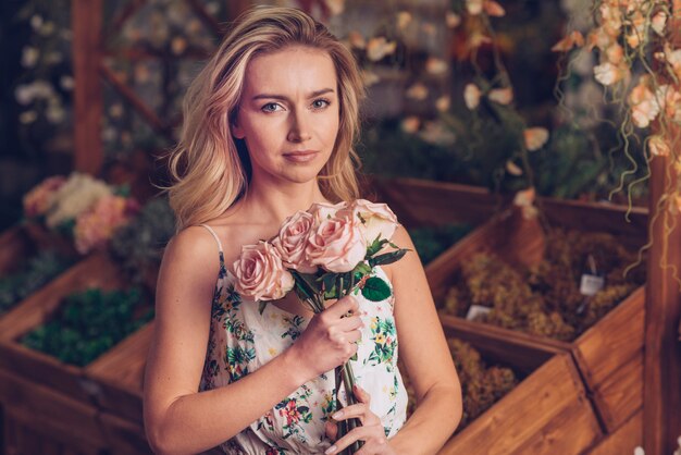 Retrato de una mujer joven seria que sostiene rosas rosadas disponibles