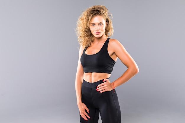 Retrato de mujer joven sexy con las manos en las caderas. Mujer fitness con cuerpo musculoso listo con guantes de mano para entrenamiento en pared gris