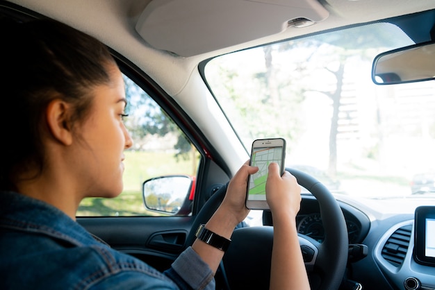 Retrato de mujer joven con sistema de navegación GPS en su teléfono móvil mientras conduce su coche