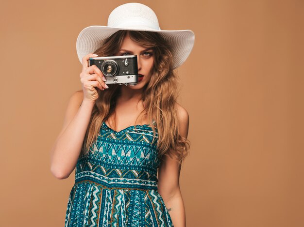 Retrato de mujer joven sonriente alegre tomando fotos con inspiración y vestido de verano. Chica sosteniendo la cámara retro. Modelo posando en sombrero